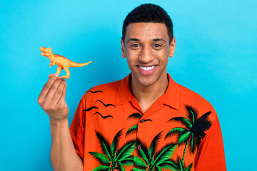 Photo of funky cheerful guy dressed print shirt rising small plastic dino toy isolated blue color background
