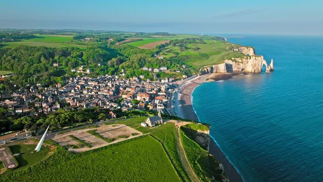 Aerial view of French traditional houses by the towering cliffs and natural arch in Etretat in France. Rock formation by the water edge, scenic point tourist attraction. Scenic view of Falaise d'Aval.