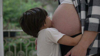 Cute little boy hugging mother's pregnant belly showcasing love and affection during late stage of...