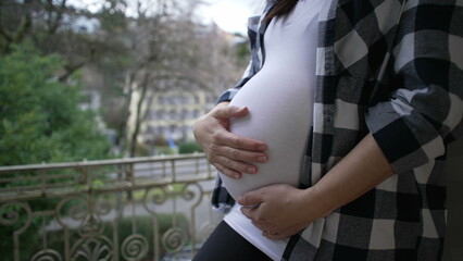 Pregnant mother caressing 8 month belly by apartment balcony showing love and affection expecting...
