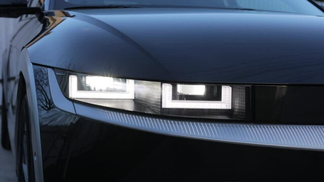 Headlight turning on switching of car LED headlights in night. New modern electric car headlamp. Close up of car front iq led light with a blurry background