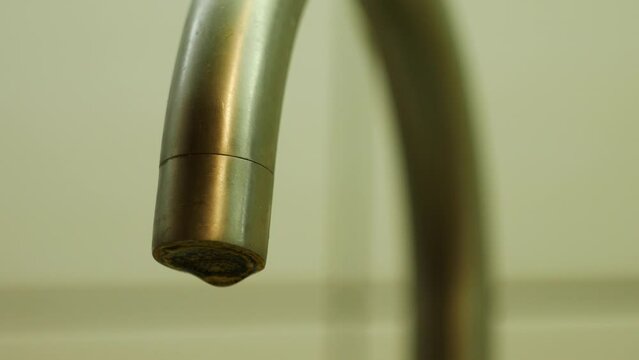 Water slowly drips from a curved metal kitchen faucet. Close-up video focusing on the faucet.