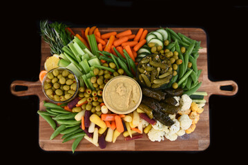High angle shot of a wooden appetizer board filled with  full of  assorted begetables, and hummus.