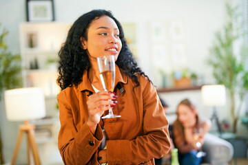 A radiant woman with a warm smile holding a champagne flute, exuding elegance and joy at a casual social gathering.