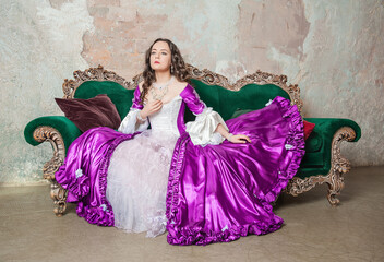 Young serious beautiful woman in fantasy rococo style medieval dress sitting on the sofa
