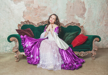 Young smiling beautiful woman in fantasy rococo style medieval dress sitting on the sofa