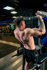 Fototapeta na wymiar in the gym a young handsome guy with tattoos is doing pull-ups on the horizontal bar shaking his back and arms