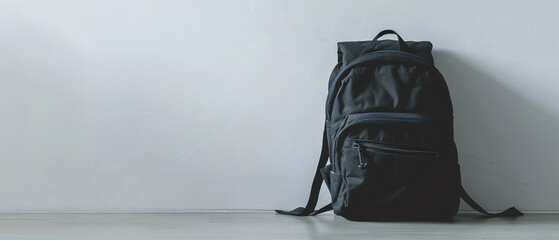 A simple black backpack hanging on a white wall, minimalist design in a modern setting. - obrazy, fototapety, plakaty