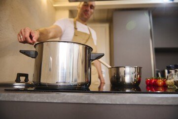 Selective focus on a stainless steel saucepan on induction cooker chef preparing food in the modern...