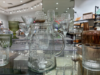 A pitcher with a floral design sits on a table next to a variety of glasses - obrazy, fototapety, plakaty
