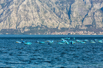 Obraz premium Mussel farm in Kotor Bay, blue nets, mountain backdrop, clear skies. Kostanjica, Kotor, Montenegro