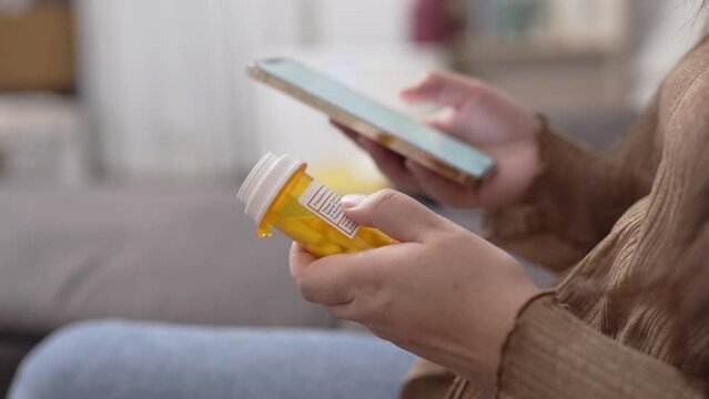 Close up woman holding prescription pill bottles and using smartphone searching online information about medicament