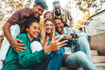 Group of multiracial young people using smart mobile phone device outdoors - Happy university students watching cellphones sitting in college campus - Teenagers addicted to social media technology