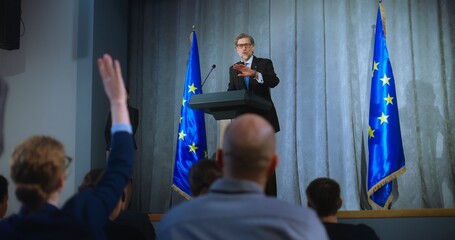 Confident politician makes an announcement, delivers campaign speech, gives interview to journalists and media. Mature representative of the European Union performs at press conference. Election day. - obrazy, fototapety, plakaty
