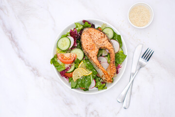 Grilled salmon and fresh vegetables: tomatoes, cucumber, lemon, radish on bricks background.
