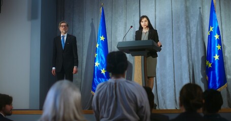 Obraz premium Female politician comes to tribune, delivers campaign speech, answers journalists questions, gives interview to media. Representative of the European Union performs at press conference. Elections day.