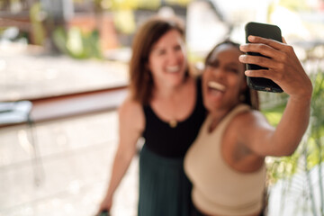 Joyful multicultural friends, a Caucasian and an African American woman in their 20s, take a blurred selfie on a bright day, reflecting the spontaneity of life. Social media photos, camera quality
