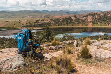 blue hiking backpack placed on the rocks in the mountain surrounded by green vegetation and natural...