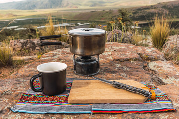 camping pots and stove and cutting board with a knife and black cup placed on the vegetation in the...