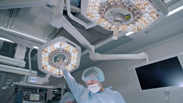 A surgeon is adjusting a surgical light in an operating room, within a building, to provide better illumination for the procedure.