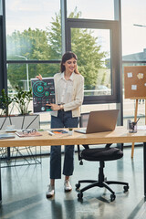 A businesswoman stands in a modern office, focusing on her laptop at a stylish desk, showcasing the franchise concept.