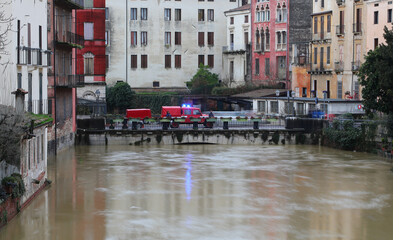 Firefighting vehicles and swollen river during flood, water lapping at houses about to overflow