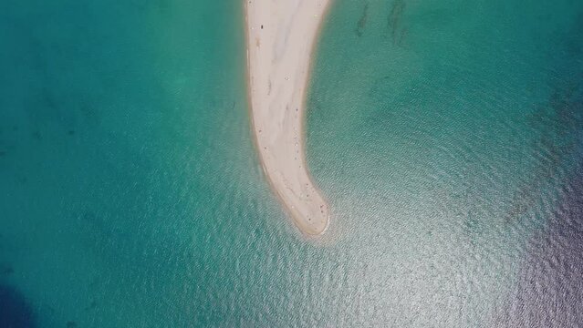 Over Cape Possidi, Halkidiki, Greece, a drone moves forward, capturing a narrow sandbar with beachgoers and shallow waters on both sides