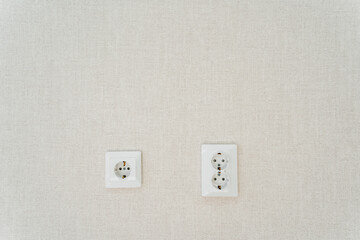 Two white wall sockets shaped like rectangles hang on the white wall