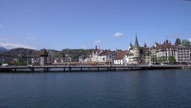 Arriving at pier of Swiss City of Lucerne with famous covered wooden Kappel Bridge and water tower in the background on a sunny spring day. Movie shot April 11th, 2024, Lucerne.