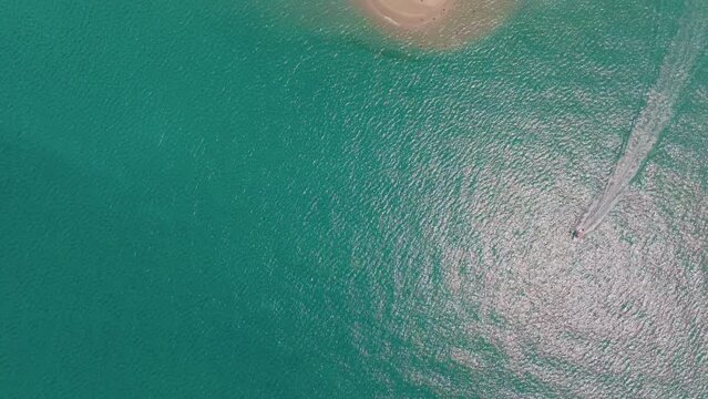 Drone advances over the sea capturing a boat moving through the water near the sandbar of Possidi Cape, Halkidiki, Greece