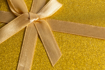 Gold gift box with ribbon and bow on shiny gold background. Top view.