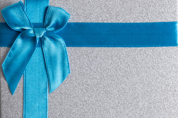 Gift box with blue satin ribbon and bow on grey background.
