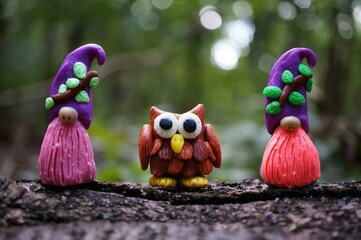 Figurines of small colorful gnomes and an owl. Fairy-tale characters in the forest.