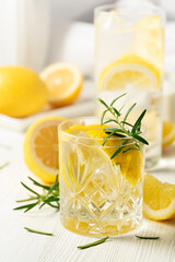 Summer refreshing lemonade drink or alcoholic cocktail with ice, rosemary and lemon slices on the white table.