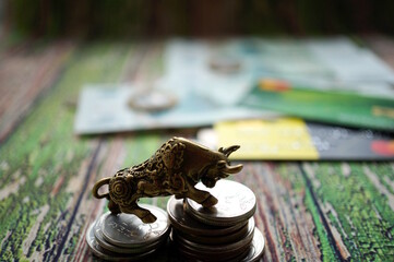 A metal bull figurine with coins on the table. Finance and economics.