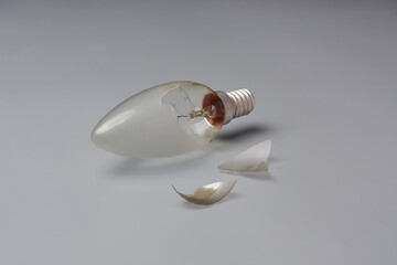 broken incandescent light bulb with pieces isolated gray background, exposed filament materials and...