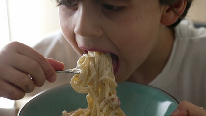 Child eating pasta, hungry 5 year old little boy eats carb food, kid enjoying cheese spaghetti,...