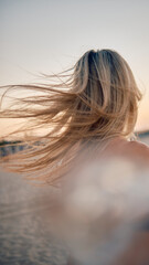 An evocative scene with a blonde woman's windswept hair by the seaside at golden hour capturing...