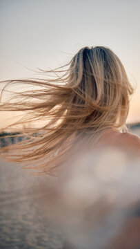 An evocative scene with a blonde woman's windswept hair by the seaside at golden hour capturing movement and natural beauty
