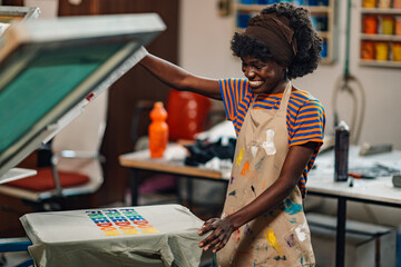 Smiling interracial printing shop worker silk screen printing on t-shirt