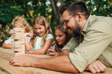 Father is playing jenga game with his family in nature.