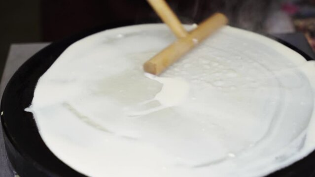 A skilled chef expertly prepares a thin crepe on a hot griddle, flipping it with precision in a bustling Paris cafe.