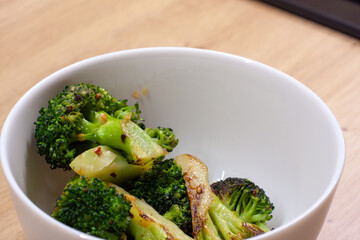 The white bowl with stir-fried broccoli on the wooden table 