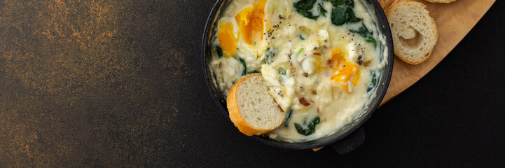 Healthy breakfasts or dinners banner, fried eggs with cheese, spinach leaves and coconut milk in a cast-iron pan, sliced baguette on a cutting board on a brown background - obrazy, fototapety, plakaty
