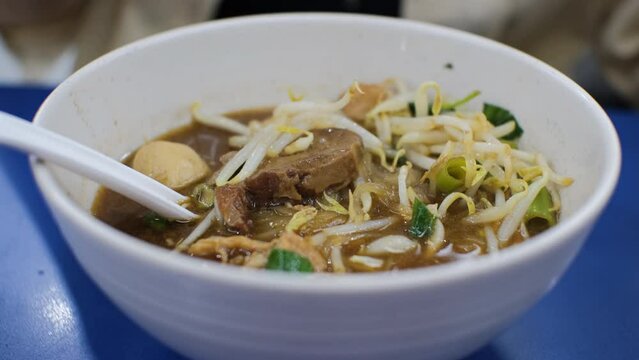 Close-up of female eating bean sprouts from tasty Guay teow noodle soup in cafe. Traditional Thai food concept