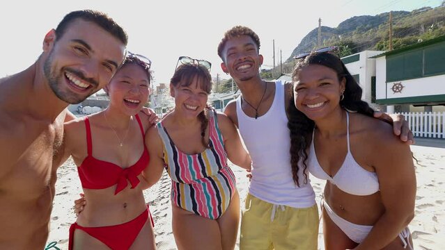 Smiling portrait of diverse friends looking at camera hugging each other at beach party during summer vacation. Friendship and holidays concept.