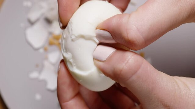 Female hands crack a boiled chicken egg into two halves, top view against the backdrop of the shell.