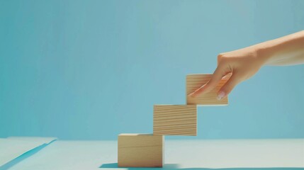 Behold a visual representation of business success and growth, as a woman's hand delicately arranges wood block stacking to form step stairs on a paper blue background.