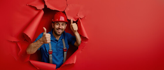 Fototapeta premium Optimistic worker popping through yellow wall Optimistic worker popping through yellow wall Optimistic worker with thumbs up emerging from bright red paper wall, wearing helmet and coveralls