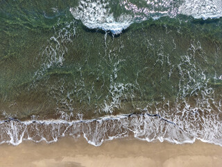 Drone view of the sandy beach and the waves on the sea on a sunny day, top view. Summer seascape from the air. Concept and idea of travel